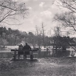 Rear view of men sitting on riverbank against sky