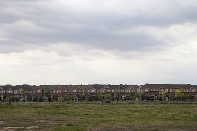 Houses on field against cloudy sky