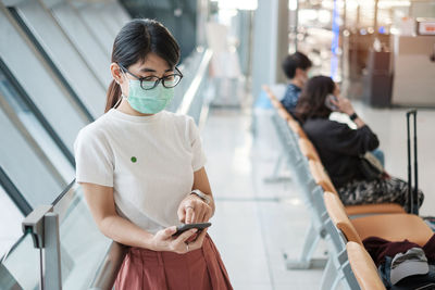 Woman holding mobile phone while standing on laptop