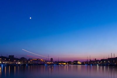 Illuminated city by river against sky at dusk