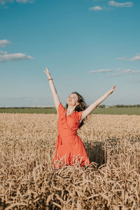 Woman with arms raised on field against sky