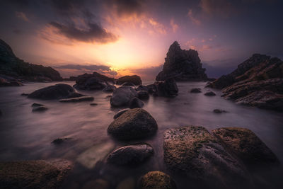 Rocks on sea shore against sky during sunset