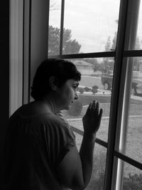 Side view of woman looking through window at home