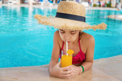 Girl drinking orange juice at pool side
