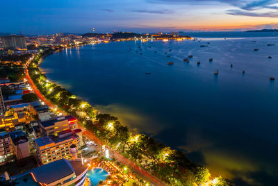 High angle view of illuminated buildings by sea against sky at sunset