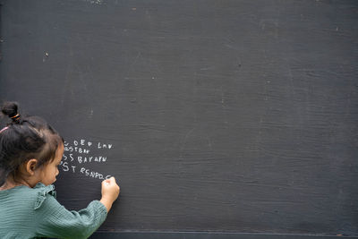 Portrait of cute girl writing alphabet on blackboard