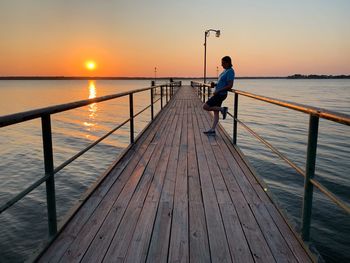 Man on pier over sea against sky during sunset