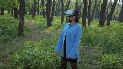 Woman wearing virtual reality simulator while standing on field at forest