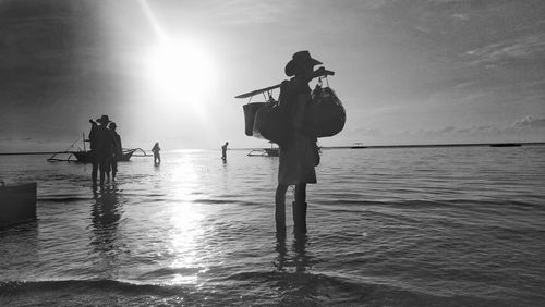 Silhouette people standing in sea against sky