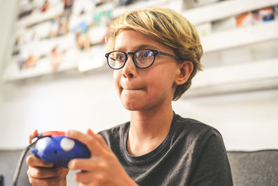 Boy playing video game while sitting on sofa in living room at home