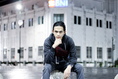 Portrait of young man sitting against building in city