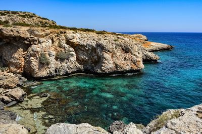 Rock formations by sea against clear blue sky