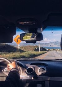 Low section of man driving car on road against sky