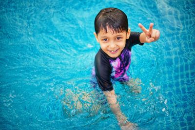 Portrait of smiling boy gesturing while standing in swimming pool