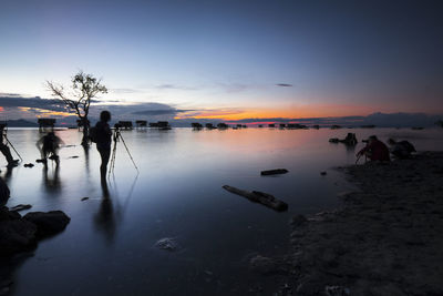 Silhouette man and woman photographing sea during sunset