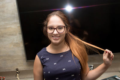 Portrait of smiling young woman against television set at home