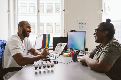 Cheerful male doctor and woman talking while sitting at desk in medical clinic