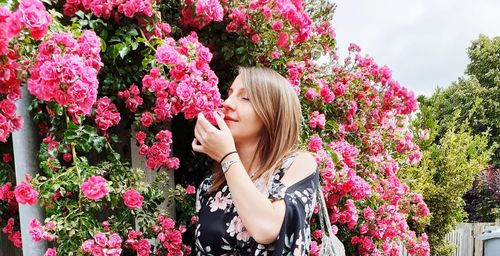 Low section of woman standing by pink flowering plants