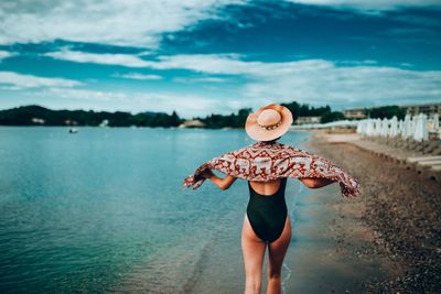 Rear view of woman standing by sea against sky