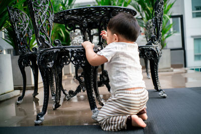 Cute boy crouching by chair outdoors