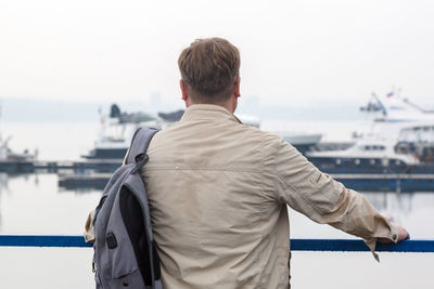 A man with a backpack in a wet jacket is waiting for his ship in the rain.