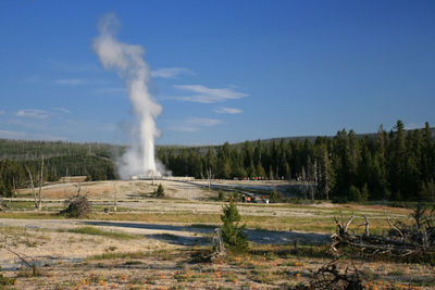 People visit old faithful geyser eruption in yellowstone national park against blue sky