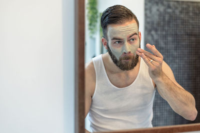 Young man applying facial cream while looking into mirror at home