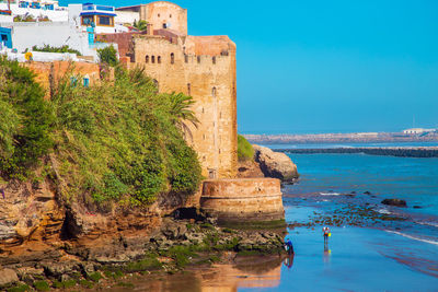 Castle with people at beach by sea against blue sky