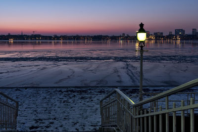 View of illuminated city by sea against sky during sunset