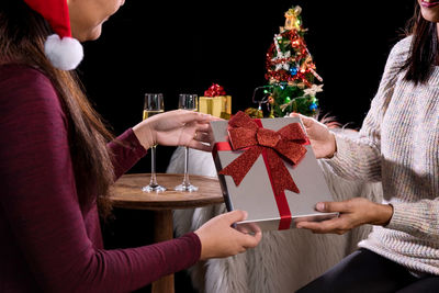 Midsection of woman receiving gift from friend over black background