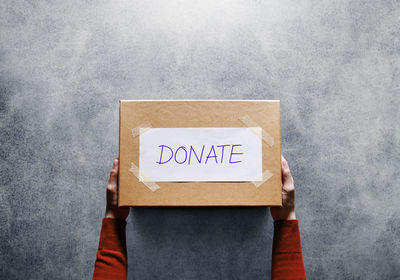 Cropped hands holding cardboard box with donate text on table