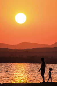 Silhouette men on sea against orange sky