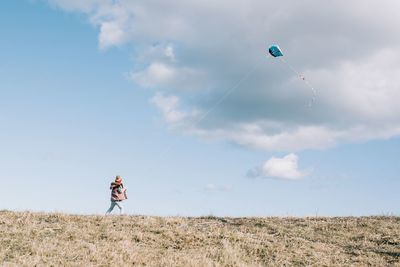 Girl flying a kite at the top of a hill with a fluffy cloud sky