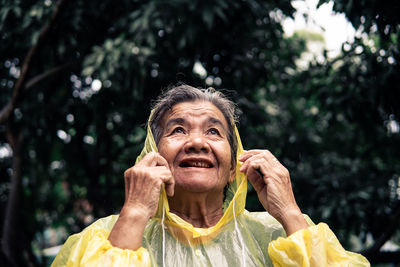 Close-up of thoughtful senior woman wearing raincoat against trees