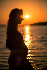 Silhouette woman standing against sea during sunset