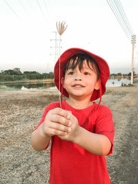 Portrait of boy holding red umbrella against sky