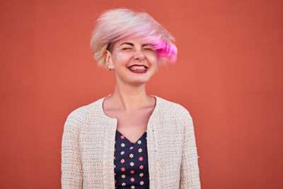 Carefree alternative female throwing dyed short hair against orange wall in urban area