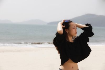 Beautiful young woman standing at beach against sky