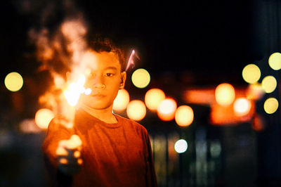 Portrait of man standing against illuminated lights at night