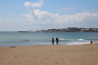 Surfers at beach against sky during sunny day