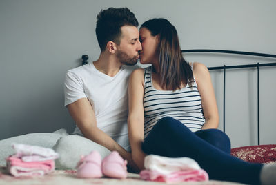 Man kissing pregnant women while sitting on bed at home