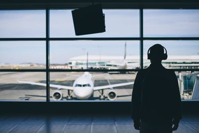 Rear view of man looking at airplane through window