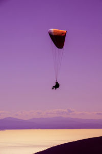 Low angle view of silhouette people paragliding against dramatic sky during sunset