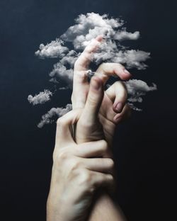 Close-up of person holding hands against black background