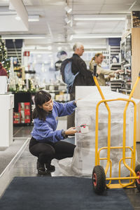 Saleswoman packing appliance while crouching in store