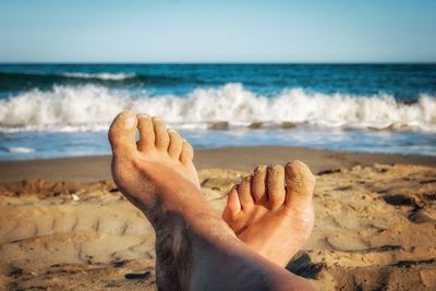 Low section of man relaxing at beach against clear sky during sunset