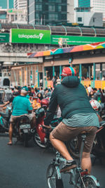 Rear view of people riding bicycle on city street