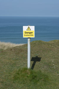 Information sign on shore by sea against sky