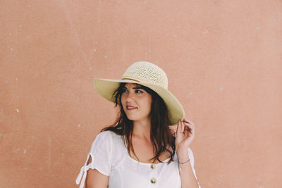 Portrait of beautiful young woman wearing summer clothes, standing in front of pastel orange wall