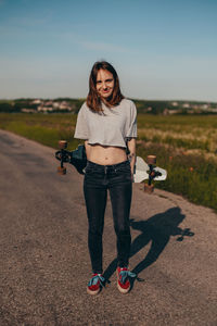 Full length of woman holding skateboard against sky